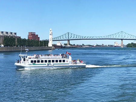 Navette fluviale de Montréal navigant sur le fleuve Saint-Laurent avec la tour de l'horloge et le pont Jacques Cartier en arrière plan