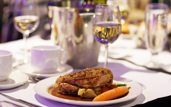 Une assiette bistronomique comprenant un suprême de volaille manchon, des pommes de terre grelots et des légumes frais du marché accompagné d'un verre de vin blanc.