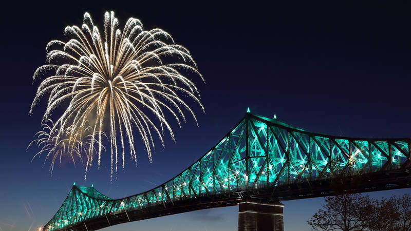 A golden firework lights up the night sky next to an iconic bridge illuminated with turquoise lights, creating a festive and spectacular scene.