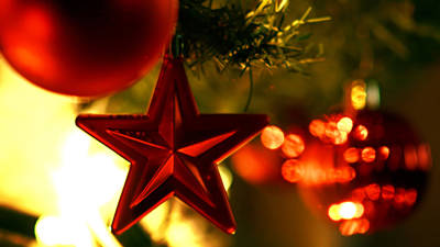 Close-up of a shiny red star hanging on a Christmas tree, surrounded by other red ornaments and lit by warm lights.