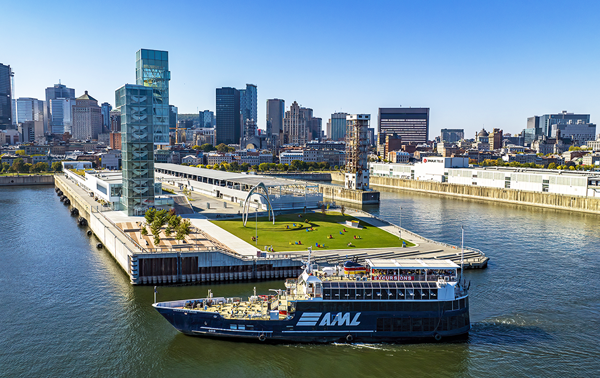 Aerial view of the AML Cavalier Maxim parked in front of the Port of Montreal Tower by day, with a view of the city's sunny skyline in the background.