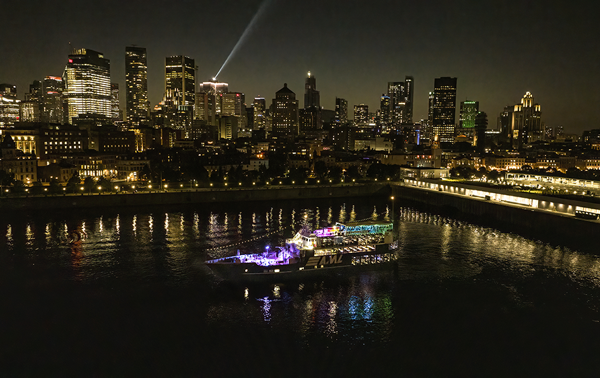 Aerial view of the AML Cavalier Maxim parked in Montreal's Old Port at night, with the city skyline in the background.