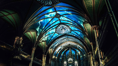 Impressive view of the vaulted Gothic-style ceiling of Notre-Dame Basilica in Montreal with a celestial blue light projected as part of the AURA cultural experience.