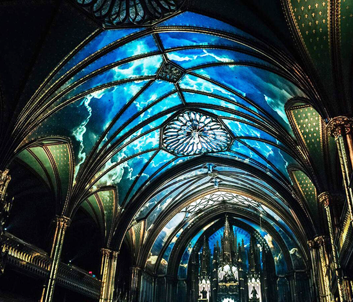Impressive view of the vaulted Gothic-style ceiling of Notre-Dame Basilica in Montreal with a celestial blue light projected as part of the AURA cultural experience.
