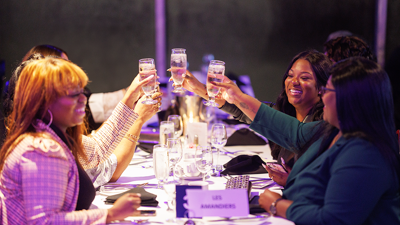 A group of smiling women clinking champagne glasses at a table during a dinner cruise aboard the AML Cavalier Maxim in Montreal.