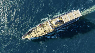 Aerial view of a cruise ship sailing on blue waters, with passengers on the deck enjoying the trip.
