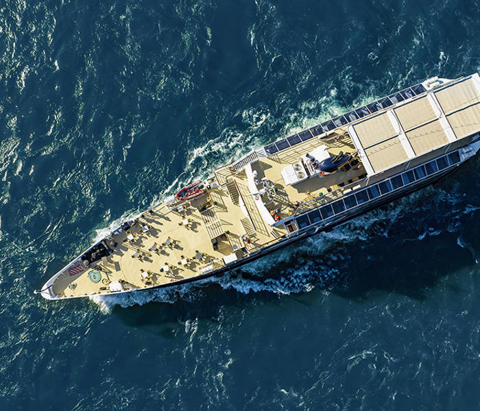 Aerial view of a cruise ship sailing on blue waters, with passengers on the deck enjoying the trip.