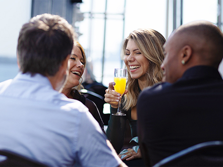 Un groupe de quatre amis partage un moment joyeux dans un restaurant près de l'eau, une femme souriante tient un verre de mimosa.