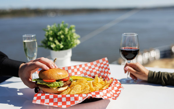 Two people enjoying a burger with fries, each with a glass of wine, on one of the terraces of the AML Cavalier Maxim in Montreal.
