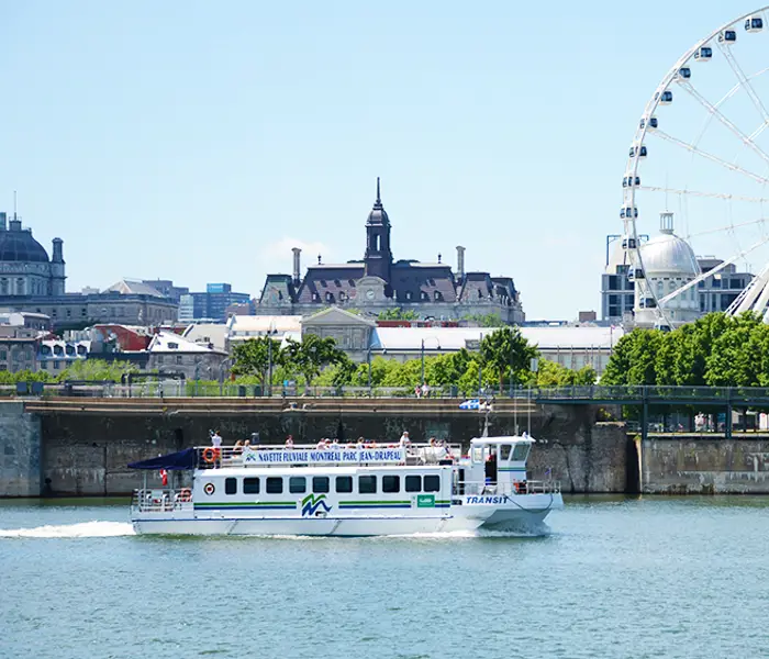 Une vue d'un bateau naviguant sur le fleuve devant une grande roue emblématique, avec des bâtiments historiques et modernes en arrière-plan sous un ciel bleu.