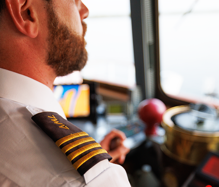 Un capitaine de navire en uniforme, vu de dos, surplombe l'équipement de navigation et le fleuve Saint-Laurent depuis le pont d'un navire.
