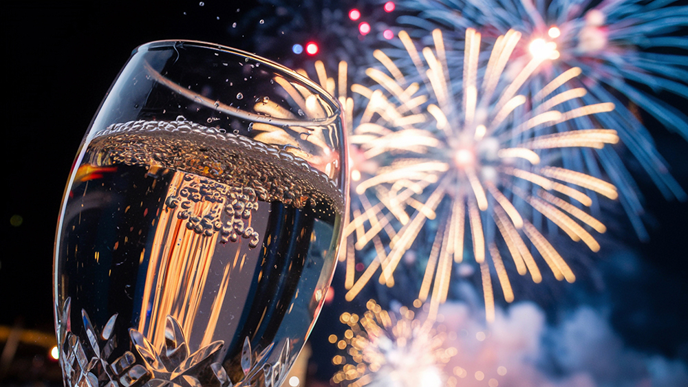Un gros plan d'une flûte de champagne pétillant au premier plan, avec des feux d'artifice éclatants illuminant le ciel nocturne en arrière-plan.
