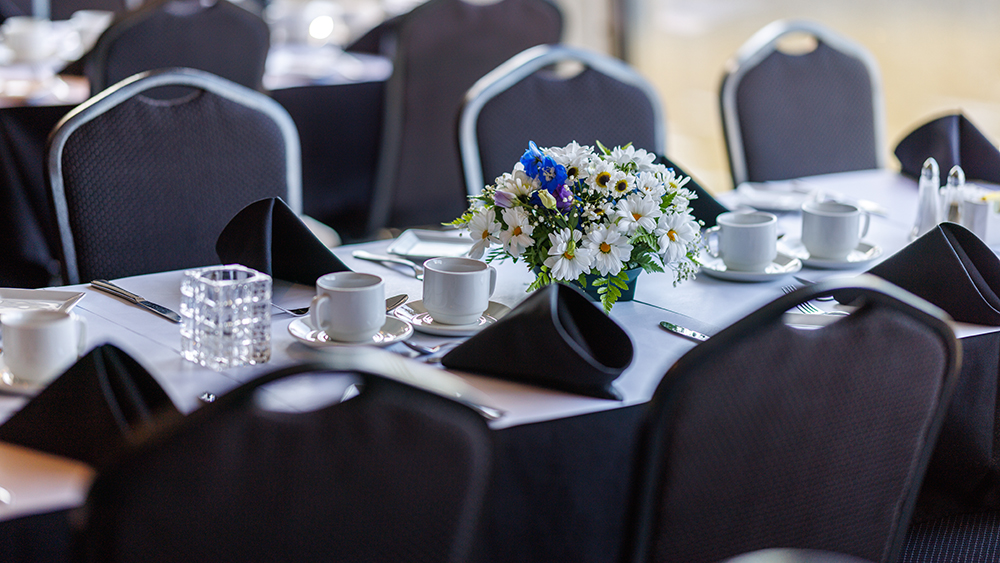 Close-up of a set table, with plates, glasses, cutlery, and a beautiful white and blue bouquet as decoration.