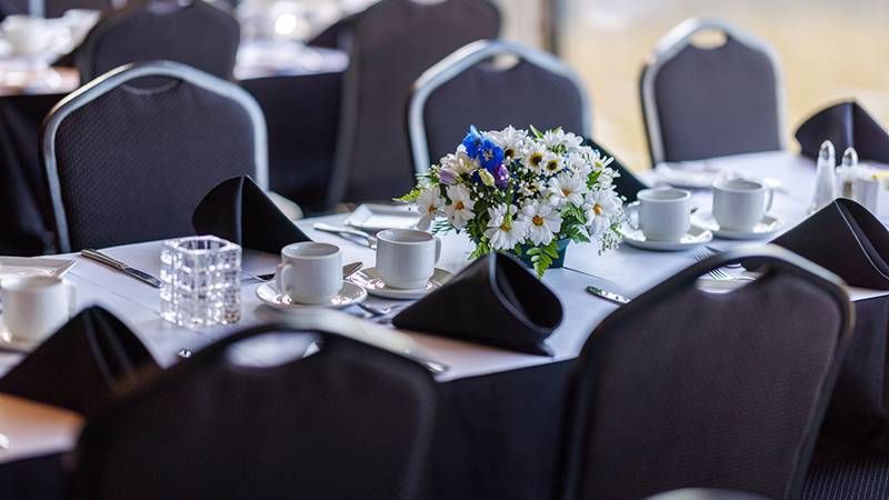 Gros plan sur une table dressée, avec des assiettes, des verres, des couverts, et un beau bouquet blanc et bleu en guise de décoration