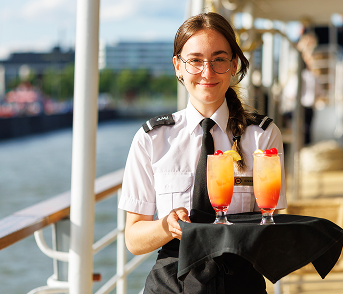 A waitress holding a tray with orange cocktails on the outdoor terrace of the AML Cavalier Maxim ship in Montreal.
