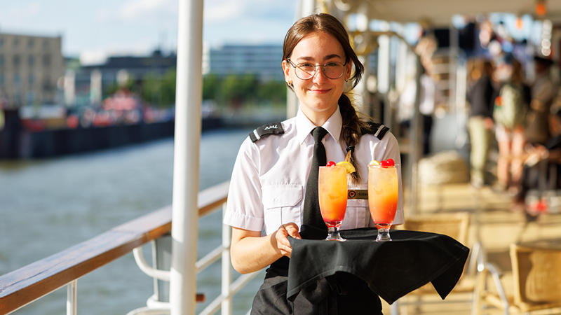 A waitress holding a tray with orange cocktails on the outdoor terrace of the AML Cavalier Maxim ship in Montreal.