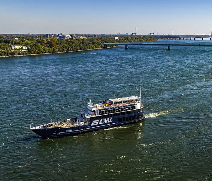 Aerial view of a cruise ship sailing on a river, with a large white clock tower in the foreground and a bridge in the background under a clear sky.