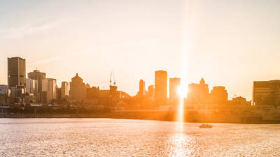 A city skyline bathed in golden sunset light, with skyscrapers in the background and a shimmering river in the foreground.