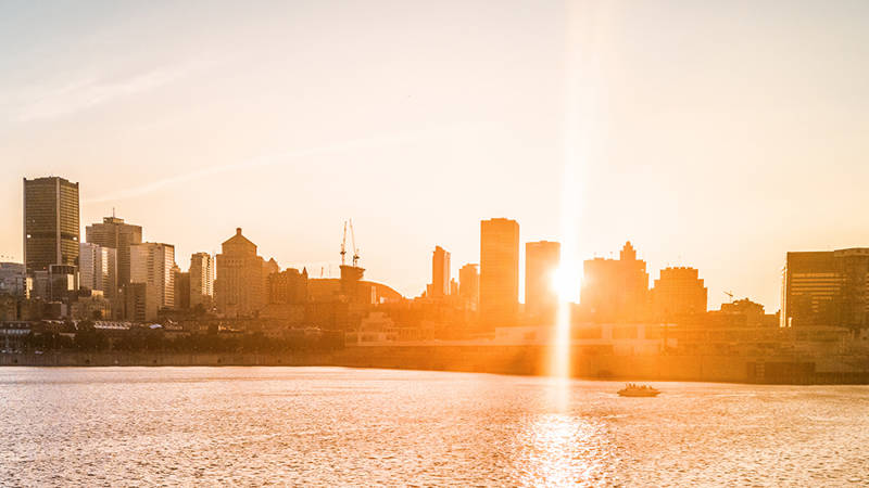 A city skyline bathed in golden sunset light, with skyscrapers in the background and a shimmering river in the foreground.