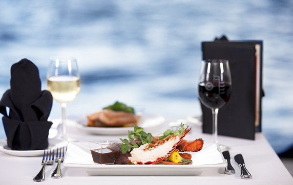 Une assiette de homard, un verre de vin blanc et du vin rouge sur une table avec vue sur le Saint-Laurent à Montréal.