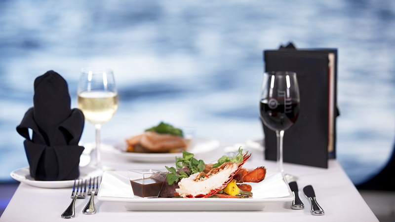 Une assiette de homard, un verre de vin blanc et du vin rouge sur une table avec vue sur le Saint-Laurent à Montréal.