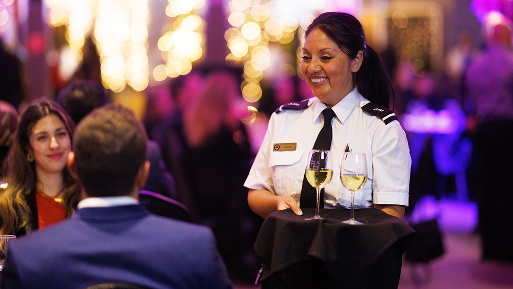 A smiling waitress in uniform serving champagne to guests during a dinner cruise on the AML Cavalier Maxim ship in Montreal.