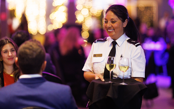 Une serveuse souriante en uniforme servant du champagne aux invités lors d'un souper-croisière sur le navire AML Cavalier Maxim à Montréal.