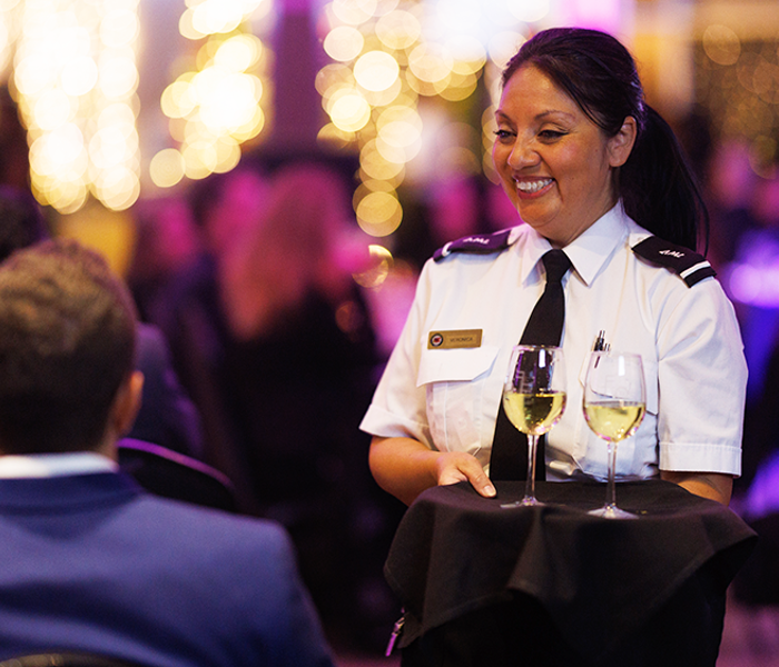 A smiling waitress in uniform serving champagne to guests during a dinner cruise on the AML Cavalier Maxim ship in Montreal.