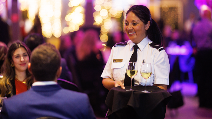Une serveuse souriante en uniforme servant du champagne aux invités lors d'un souper-croisière sur le navire AML Cavalier Maxim à Montréal.