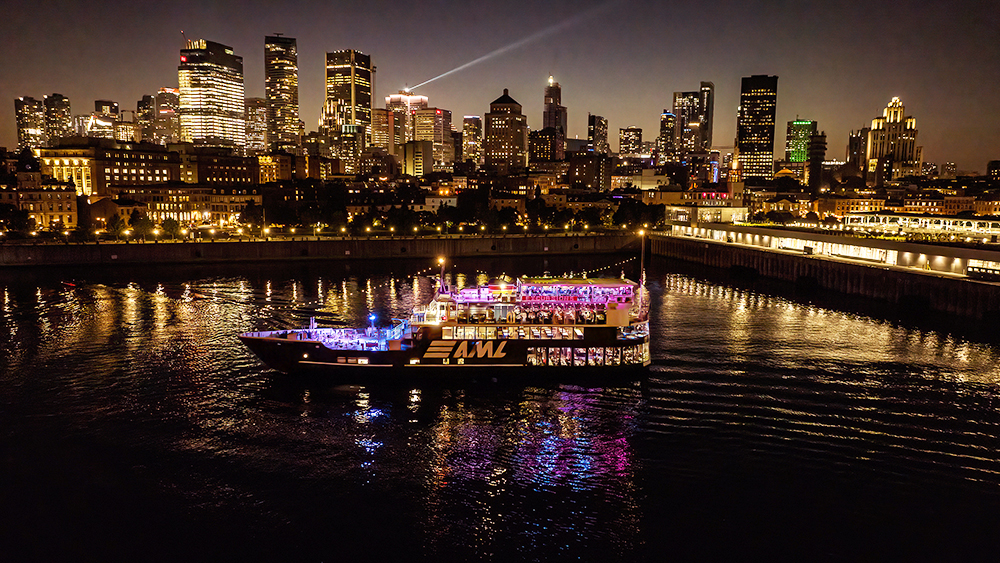 A stunning nighttime view of an illuminated cruise ship sailing on a river, with a sparkling city skyline in the background featuring skyscrapers and urban lights.
