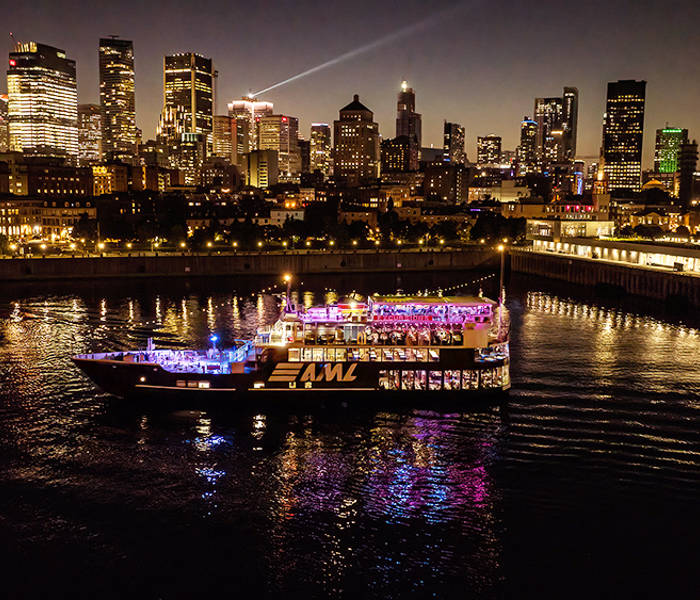 A stunning nighttime view of an illuminated cruise ship sailing on a river, with a sparkling city skyline in the background featuring skyscrapers and urban lights.