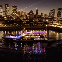 Un groupe de quatre amis souriants trinque avec des cocktails colorés sur une terrasse, avec des gratte-ciel en arrière-plan.