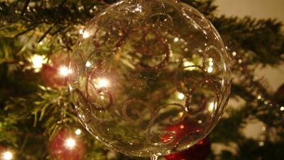 Close-up of a transparent Christmas ornament with golden patterns, hanging on a decorated tree with lights and ornaments.