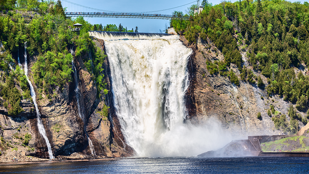 Chute Montmorency en été se jetant dans la rivière Montmorency en contrebas, entourée d'arbres avec une passerelle suspendue au-dessus