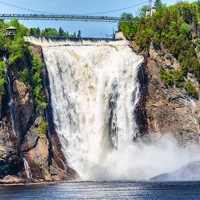 Montmorency Falls in the summer cascading into the Montmorency River below, surrounded by trees with a suspended footbridge above