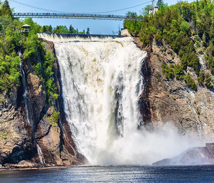 Chute Montmorency en été se jetant dans la rivière Montmorency en contrebas, entourée d'arbres avec une passerelle suspendue au-dessus