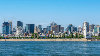View of the Montreal skyline with a blue sky in the background and the glittering St. Lawrence River in the foreground.