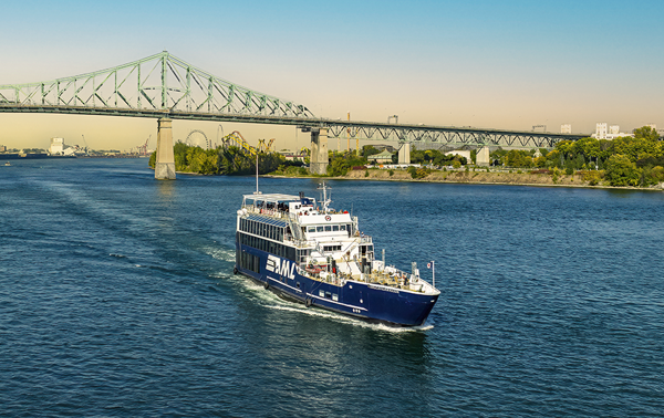 The AML Cavalier Maxim in the foreground, sailing on the St. Lawrence River with a view of the Jacques Cartier Bridge in the background.
