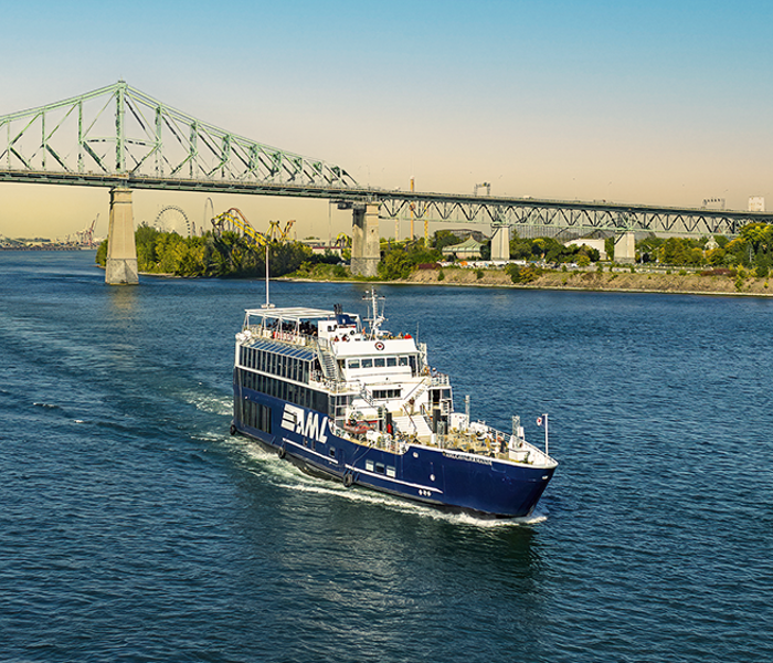 The AML Cavalier Maxim in the foreground, sailing on the St. Lawrence River with a view of the Jacques Cartier Bridge in the background.