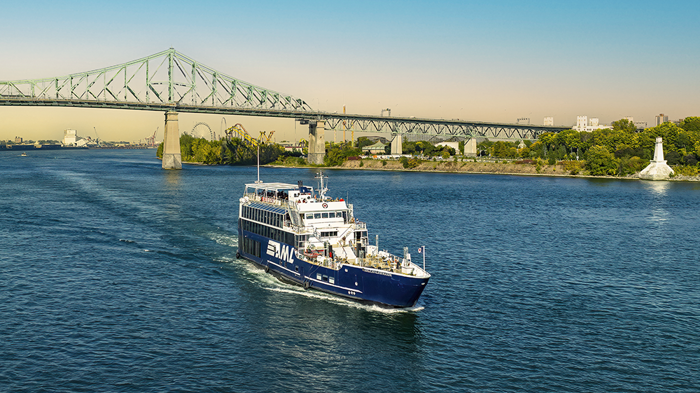 Le navire AML Cavalier Maxim au premier plan naviguant sur le fleuve Saint-Laurent avec une vue sur le Pont Jacques Cartier en arrière plan.