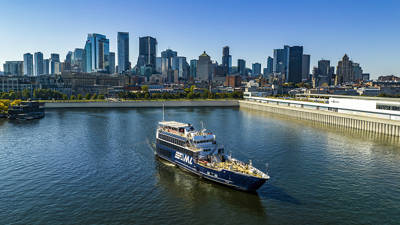 A cruise ship sailing on a river, with a panoramic view of a city skyline featuring tall skyscrapers in the background under a clear sky.