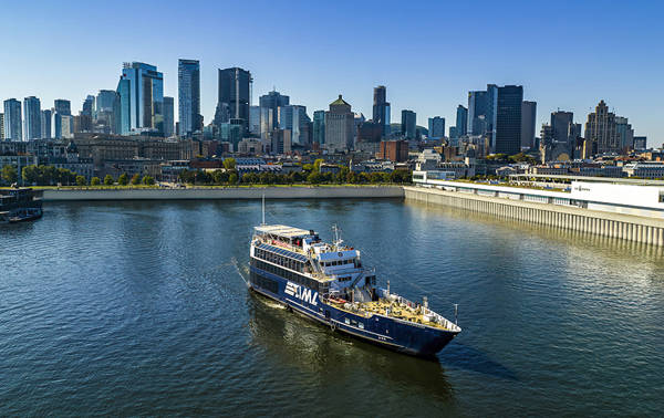 A cruise ship sailing on a river, with a panoramic view of a city skyline featuring tall skyscrapers in the background under a clear sky.