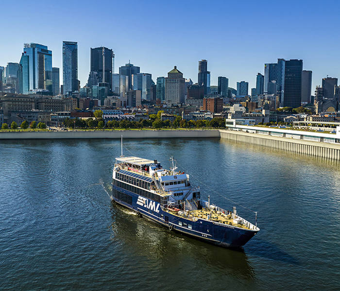 A cruise ship sailing on a river, with a panoramic view of a city skyline featuring tall skyscrapers in the background under a clear sky.