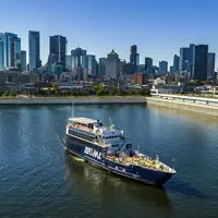 Un bateau de croisière naviguant sur une rivière, avec une vue panoramique sur une ville avec de hauts gratte-ciels en arrière-plan sous un ciel dégagé.