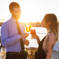 A smiling and affectionate couple enjoying a cocktail on the terrace of the AML Cavalier Maxim ship in Montreal, with a sunset in the background