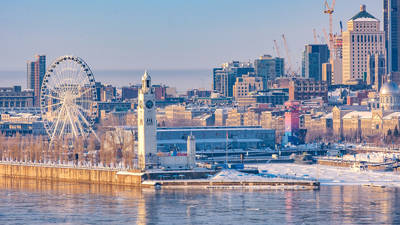 Panoramic view of Old Port of Montreal in winter, featuring the Clock Tower, the Ferris wheel, and downtown buildings under a clear sky.