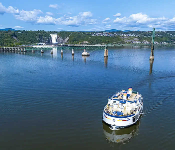 Vue aérienne du navire AML Louis Jolliet naviguant sur le fleuve Saint-Laurent avec le pont de l'Île d'Orléans et la Chute Montmorency en arrière plan.