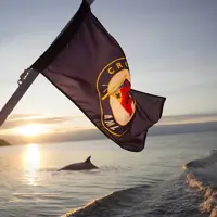 A flag flutters at the back of a boat during sunset, with calm water and the silhouette of a porpoise surfacing. The boat's wake creates a dynamic element in the serene scene.