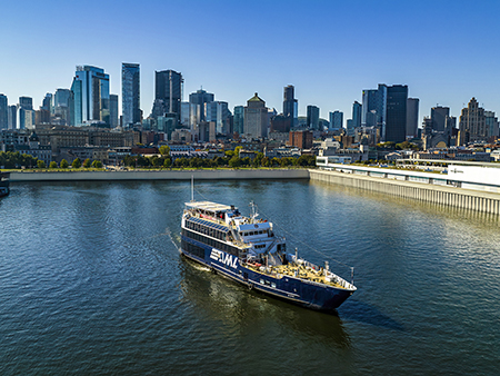 Un bateau de croisi&#xE8;re naviguant sur une rivi&#xE8;re, avec une vue panoramique sur une ville avec de hauts gratte-ciels en arri&#xE8;re-plan sous un ciel d&#xE9;gag&#xE9;.