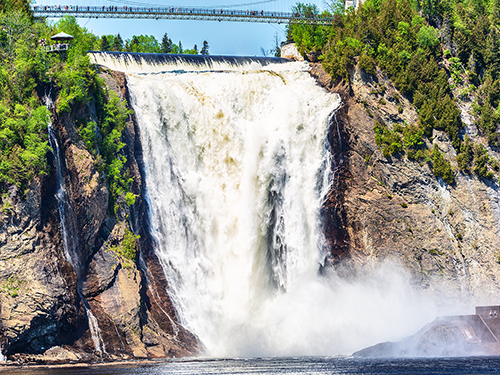 Chute Montmorency en été se jetant dans la rivière Montmorency en contrebas, entourée d'arbres avec une passerelle suspendue au-dessus